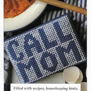 May include: A blue and white woven fabric with the word "CALL MOM" stitched in white. The fabric is on a striped background with a bowl of orange food and a wooden spoon.