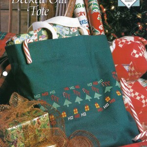 May include: A green tote bag with a cross-stitch design of Christmas trees and houses with the words "HO HO HO" repeated. The bag is filled with wrapped gifts and candy canes.