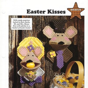 May include: Two felt mouse figures with Easter-themed decorations. The female mouse wears a yellow hat with flowers and holds a yellow candy in her mouth. The male mouse wears a brown top hat and a purple tie. The background is a wooden surface with a basket of Easter eggs.