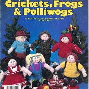 May include: A crochet pattern book featuring 12 different crochet doll patterns. The cover shows a group of dolls dressed as crickets, frogs, and polliwogs. The book title is "Crickets, Frogs & Polliwogs" and the subtitle is "12 Fantastic Frolicking Friends in Crochet".