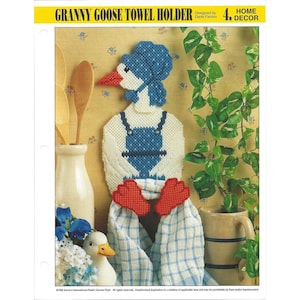 May include: A Granny Goose towel holder made of plastic canvas. The goose has a blue bonnet, overalls, and red feet. A blue and white checkered towel hangs from the feet. The text "GRANNY GOOSE TOWEL HOLDER" is at the top.