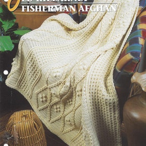 May include: A cream-colored crocheted blanket with a diamond pattern and a textured border. The blanket is draped over a chair with a brown leather armrest. The text "Old Killarney Fisherman Afghan" is printed on the image.
