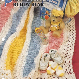 May include: A crocheted baby blanket with pastel stripes of pink, yellow, and blue. The blanket has a white crocheted border with a delicate lace pattern. A small teddy bear wearing a crocheted hat and dress is sitting on the blanket. The blanket is surrounded by other baby items, including a pair of white shoes, a baby bottle, and a small bag.