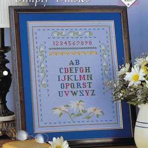 May include: Cross stitch pattern for a sampler with the alphabet, numbers 1-9, and daisies on a light blue background. The pattern is titled "Simply Daisies" and is part of the "Cross Stitch Collector's Series".