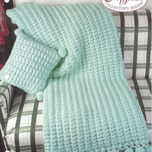 May include: A light green crochet throw blanket with a matching pillow. The blanket and pillow are made with a puffy stitch and have a fringe border. The blanket is displayed on a green and white plaid couch. The text "12-Hour Time Savers" and "Afghan Collector's Series" is printed on the top of the image. The text "Padded Puffs" and "Designed by Erma Fielder" is printed at the bottom of the image.