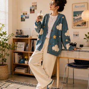 May include: A blue V-neck cardigan featuring a white cloud and yellow star pattern, worn over a white t-shirt with cream-colored wide-leg trousers and blue and white sneakers. The cardigan has a button-down front and ribbed cuffs and hem.