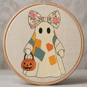 Peut inclure: Un tambour à broder contenant un tissu crème avec un personnage de fantôme brodé. Le fantôme porte un grand nœud à motifs floraux et présente des pièces colorées orange et bleu. Il tient un petit seau citrouille orange au visage noir.