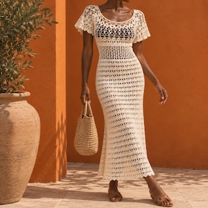 Peut inclure: Une robe longue couleur crème en crochet avec des manches courtes, une encolure dégagée et un motif ajouré complexe. Le vêtement est associé à un sac à main en paille tressée et des sandales en cuir marron, révélant une texture tricotée détaillée.