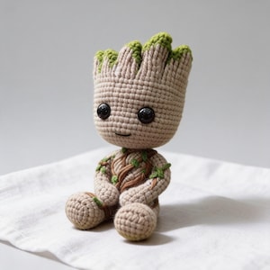 Puede incluir: Una figura amigurumi de ganchillo de un personaje parecido a un árbol con cuerpo de color tostado claro, parte superior texturizada de color verde oscuro y grandes ojos de plástico negro. La figura tiene cabeza redonda, brazos y piernas.
