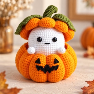 Puede incluir: Una figura de fantasma blanco tejida a ganchillo con ojos negros y una pequeña sonrisa, colocada dentro de una calabaza naranja brillante con una cara de jack-o'-lantern cosida en negro. La calabaza tiene un tallo y hojas verdes arriba.