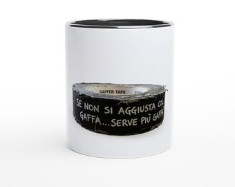May include: A white ceramic mug with a black interior rim featuring a graphic of a roll of black gaffer tape. The tape has the Italian text "SE NON SI AGGIUSTA COL GAFFA...SERVE PIÙ GAFFA" printed in white on its side, with "GAFFER TAPE" visible.