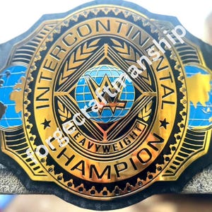 May include: A gold-plated championship belt featuring a central circular emblem with a blue globe and the text INTERCONTINENTAL HEAVYWEIGHT CHAMPION. The design includes two side globes on a black strap with intricate gold filigree and border details.