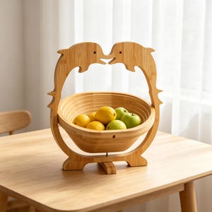 May include: A light brown bamboo fruit bowl featuring a decorative frame shaped like two dolphins facing each other. The bowl contains several yellow lemons and green apples. The structure is made of natural wood grain material with a smooth finish.