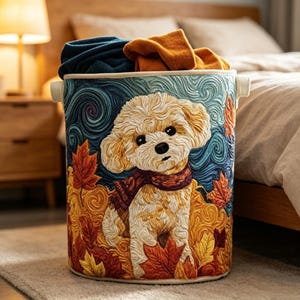 May include: A cylindrical fabric laundry basket featuring a textured illustration of a cream-colored puppy wearing a maroon scarf, surrounded by swirling blue patterns and vibrant orange and yellow autumn maple leaves, filled with folded clothing.