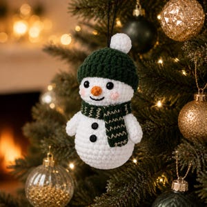 May include: A white crocheted snowman ornament featuring a dark green ribbed beanie with a white pom-pom, a matching dark green scarf with light-colored stitching, two black buttons on the torso, black bead eyes, and an orange carrot-shaped nose.