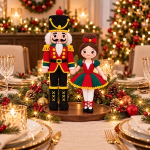 May include: A crochet nutcracker doll in a red, black, and yellow uniform standing next to a crochet ballerina doll wearing a red and green dress with a white bodice. Both dolls have detailed yarn hair and are positioned on a round wooden base.