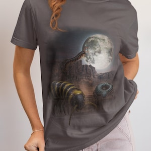 May include: A charcoal grey short-sleeve t-shirt featuring a graphic print of a desert landscape at night under a full moon. The design includes a large yellow and black striped millipede in the foreground and a smaller dark millipede nearby.