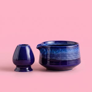 May include: A deep blue ceramic matcha whisk holder and a matching ceramic matcha bowl with a pour spout. The bowl features a gradient of dark blue at the base transitioning to a lighter, textured blue glaze near the rim, while the whisk holder is solid.