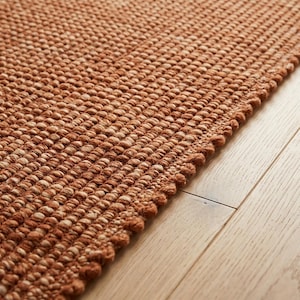 May include: A rectangular area rug featuring a dense, textured weave of terracotta and light beige fibers. The rug has a thick, knotted construction with a distinct, rounded edge detail that runs along the side, showcasing a uniform pattern.