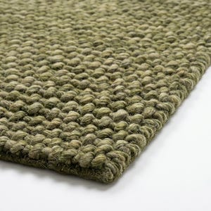 May include: A thick, hand-woven area rug featuring a chunky, textured knit pattern in a solid olive green colour. The rug displays a dense, looped construction with visible yarn fibres, creating a uniform, tactile surface across the entire piece.