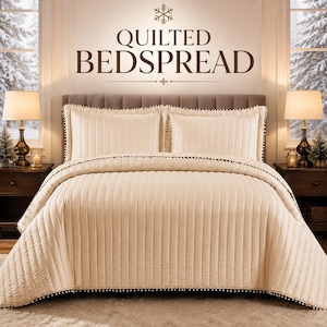 May include: A cream-coloured quilted bedspread with vertical stitching and small pom-pom trim along the edges. The set includes two matching rectangular pillow shams. The text QUILTED BEDSPREAD is centred above the bed with a snowflake icon.