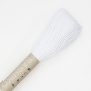 May include: A spool of white Sashiko thread, a type of Japanese embroidery thread, is displayed against a white background. The thread is tightly wound and appears soft. The label reads "SASHIKO" and "20m".