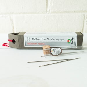May include: A package of Tulip Bullion Knot Needles, Long/Regular, with the text "Hiroshima Needle." The package is gray with a red string closure. Two needles and a cork stopper are visible.