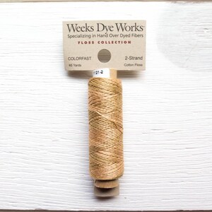 May include: A spool of Weeks Dye Works 2-strand cotton floss in a variegated tan and olive green color. The label reads "COLORFAST" and "45 Yards". The product is part of the "FLOSS COLLECTION" and is labeled with the number "1121-2".