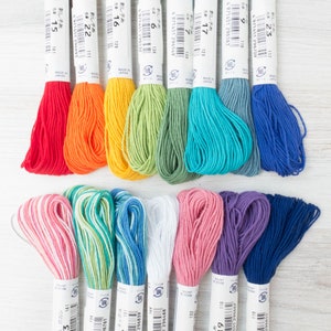 May include: A collection of colorful embroidery floss skeins in various shades, including red, orange, yellow, green, blue, and purple. Each skein is labeled with a number and made in Japan. Ideal for cross-stitch and embroidery projects.