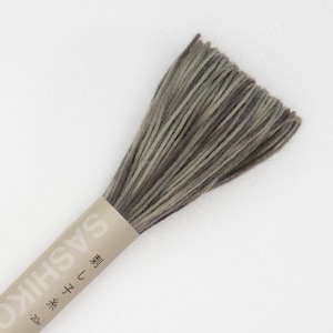 May include: A bundle of Sashiko thread in shades of gray and brown. The thread is wrapped with a tan paper label that includes Japanese text. The thread is tightly wound and ready for use in embroidery or quilting projects.