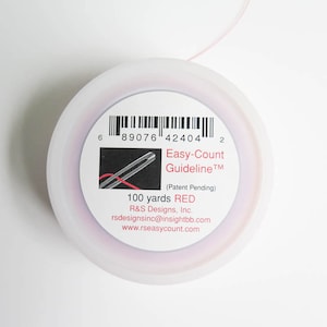 May include: A spool of red thread with the text "Easy-Count Guideline" and "100 yards RED". The spool is white with a pinkish hue and a barcode. The product is from R&S Designs, Inc.