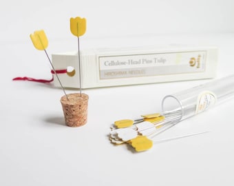May include: Cellulose-head pins with yellow tulip-shaped heads. The pins are displayed in a cork holder and a clear tube. A box with the text "Cellulose-Head Pins Tulip" and "Hiroshima Needles" is also visible. The pins are for sewing and crafting.