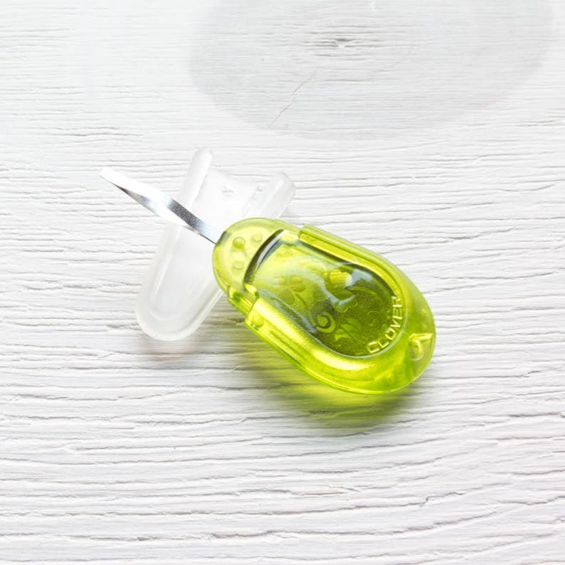 May include: A lime green Clover thread cutter with a silver blade and a clear plastic blade cover. The tool has a rounded, ergonomic design and is designed for cutting threads in sewing and crafting projects.