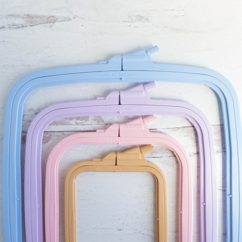 May include: Four colorful embroidery hoops in pastel shades of blue, lavender, pink, and tan, nested together. Each hoop has a measurement label in millimeters, with the largest at 280 mm and the smallest at 110 mm. The brand name "Nurge" is visible.