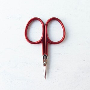 May include: Red Bohin France scissors with a silver blade. The scissors have a classic design with rounded finger holes and a pointed tip. The brand name is visible on the blade. The scissors are set against a white background.