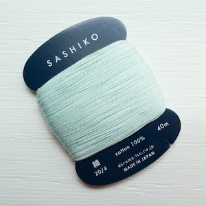 May include: A spool of light green Sashiko thread. The dark blue label reads "SASHIKO" and "cotton 100%" with "40m" and "MADE IN JAPAN". The thread is wrapped around a dark blue cardboard spool.