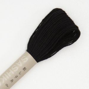 May include: A spool of black Sashiko thread, a type of Japanese embroidery thread. The thread is tightly wound and wrapped with a paper label. The label has Japanese text and the brand name "SASHIKO". The thread is approximately 20 meters in length.
