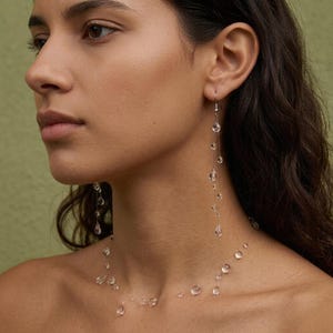 May include: A delicate jewelry set consisting of a necklace and long drop earrings. The pieces feature clear, transparent, teardrop-shaped beads suspended on a thin, nearly invisible filament, creating a floating effect around the neck and ears.