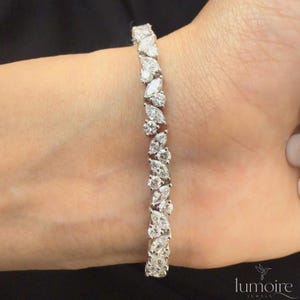 Può includere: Un bracciale color argento caratterizzato da una disposizione continua di pietre trasparenti alternate con taglio marquise e taglio rotondo. Il design presenta un motivo ripetitivo di gemme sfaccettate circolari e a forma di foglia.