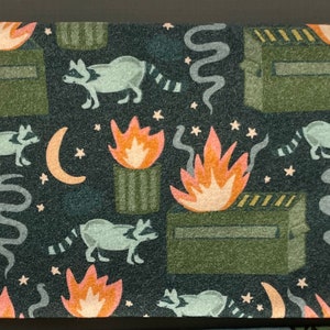 Puede incluir: Una tela verde oscura con un patr&oacute;n repetido de mapaches, fuego y botes de basura. Los mapaches son negros y blancos, el fuego es naranja y amarillo, y los botes de basura son verdes. El fondo es verde oscuro.