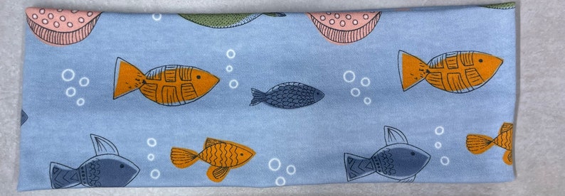 以下が含まれることがあります： オレンジとブルーの魚、ピンクとグリーンの円、白い泡が繰り返されるパターンが施された青いヘッドバンドです。