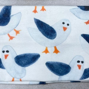 以下が含まれることがあります： 白地に青と白の海鳥が繰り返し描かれた布製のヘッドバンド。海鳥はスタイリッシュでシンプルなデザインです。