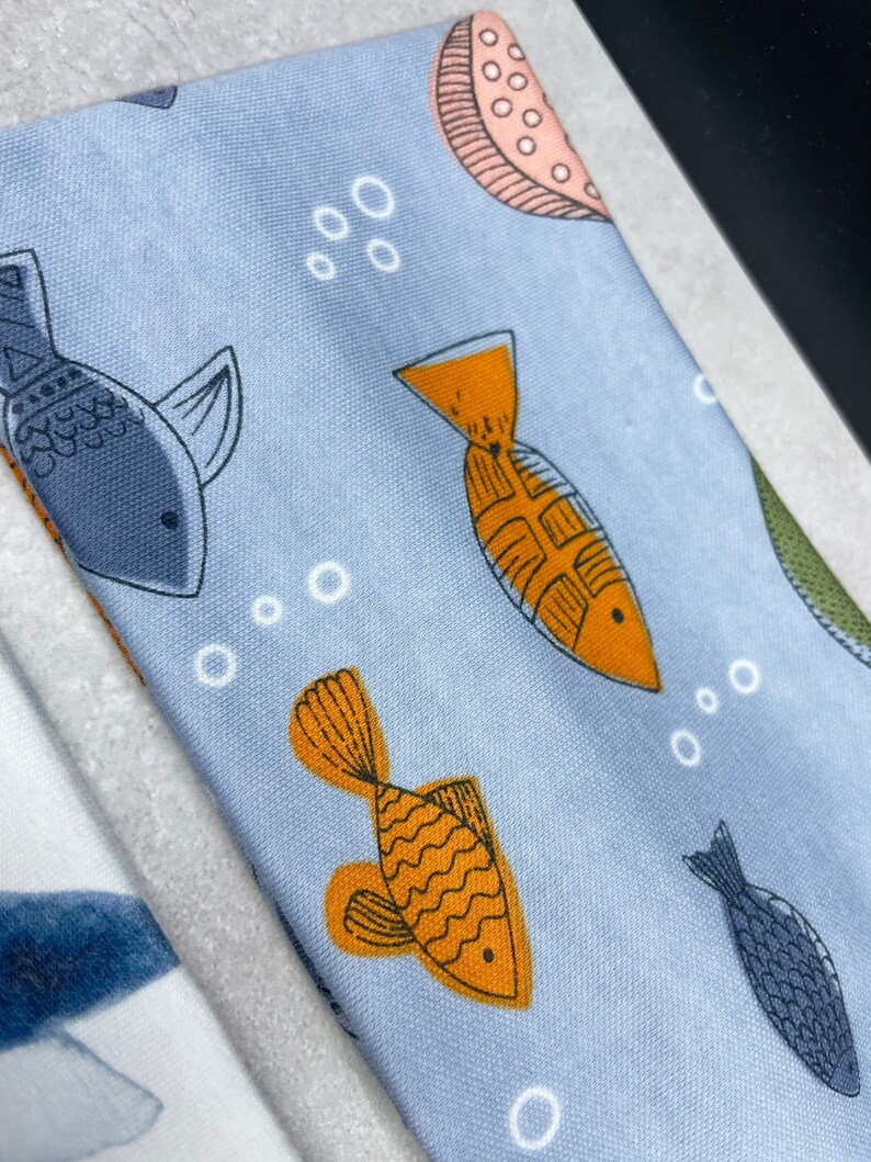 以下が含まれることがあります： オレンジとブルーの魚、白い泡、ピンクとブラウンの円形のパターンが繰り返されるライトブルーの生地。