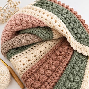 May include: A handmade crochet blanket featuring alternating horizontal stripes in dusty rose, sage green, and cream. The textile displays varied textured stitch patterns, including bobble stitches, braided cables, and simple double crochet rows.