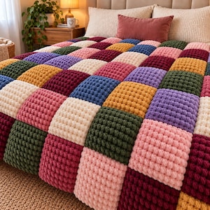 Puede incluir: Una manta de ganchillo hecha a mano con una cuadrícula de parches cuadrados en varios colores, incluyendo crema, rosa, rojo oscuro, amarillo mostaza, verde bosque y lavanda. Cada cuadrado presenta un patrón de puntos en relieve.