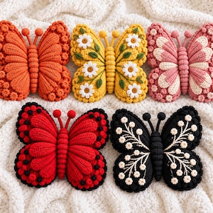 May include: Five crocheted butterfly-shaped pillows in orange, yellow with white daisies, pink and cream, red with black spots, and black with white floral embroidery. Each butterfly features a textured body, two antennae, and detailed wings.