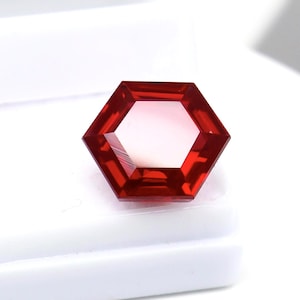 May include: A vibrant red gemstone cut into a precise hexagonal shape. The stone features multiple facets that reflect light, creating a brilliant appearance with deep crimson tones throughout the structure, showcasing a clean and symmetrical geometric design.