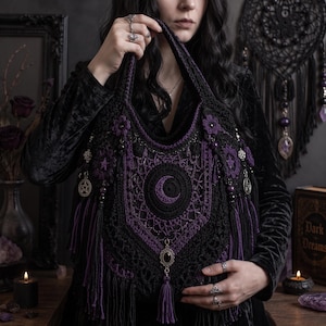 May include: A black and purple crocheted tote bag featuring a central crescent moon motif, intricate lace-like stitching, dangling tassels, and metallic charms including pentacles and a dark oval gemstone pendant hanging from the bottom center.