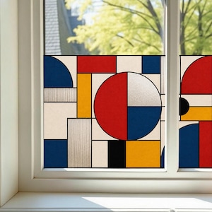 May include: A window film featuring a geometric pattern of red, blue, yellow, black, and white shapes including circles, rectangles, and squares. The design is divided by thick black lines, creating a grid-like composition on the glass surface.