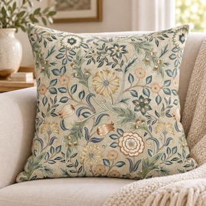 May include: A square throw pillow featuring a detailed botanical print on a beige background. The pattern consists of intricate floral motifs, including stylized flowers and leaves in shades of sage green, muted blue, soft yellow, and dusty pink.